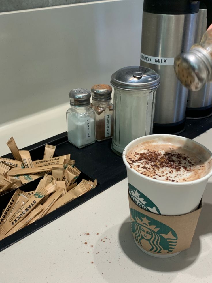 a cup of coffee sitting on top of a counter next to some sugar and cinnamon sticks