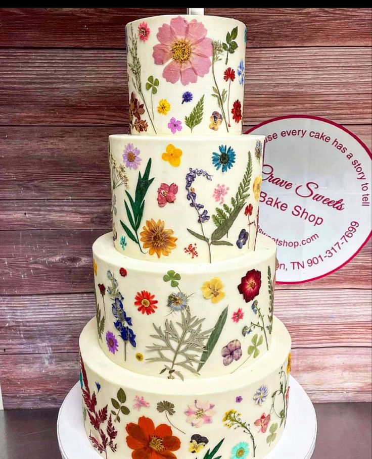 a three tiered cake decorated with flowers on a white plate next to a wooden wall