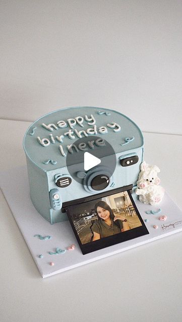 a birthday cake with a polaroid camera on it's side and a teddy bear sitting next to it