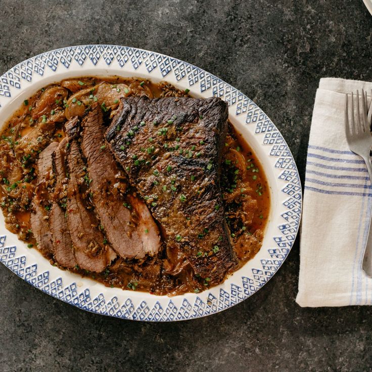 a white plate topped with meat covered in gravy next to a fork and napkin