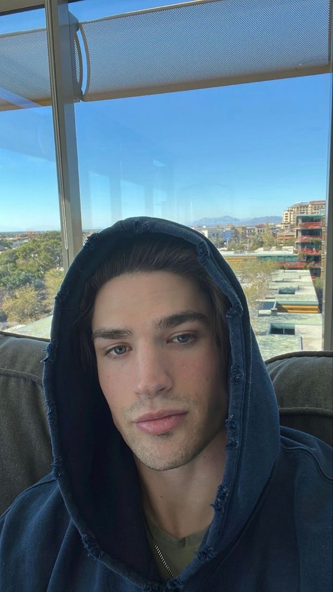 a young man wearing a hoodie looking at the camera in front of a window