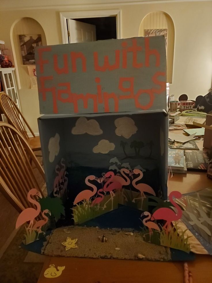 a cardboard box with flamingos on it sitting on top of a table next to chairs