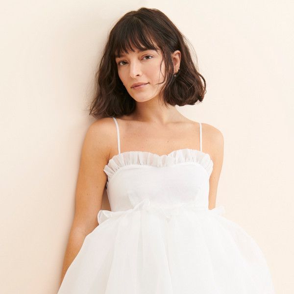 a woman in a white dress leaning against a wall