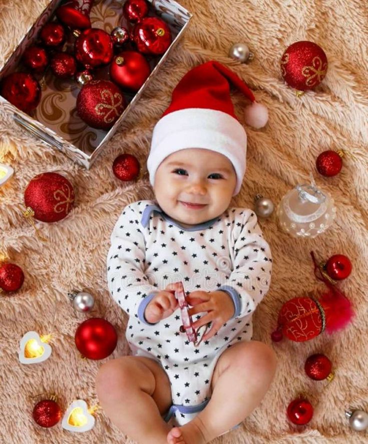 a baby wearing a santa hat sitting next to christmas ornaments