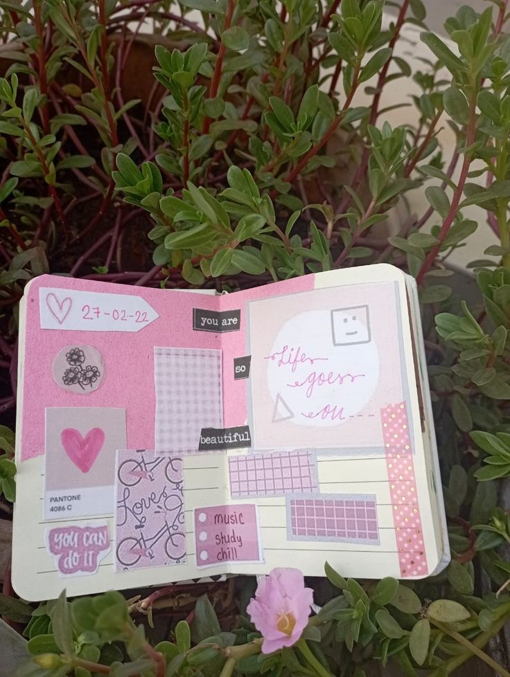 an open notebook with stickers on it sitting next to some plants and flowers in the background