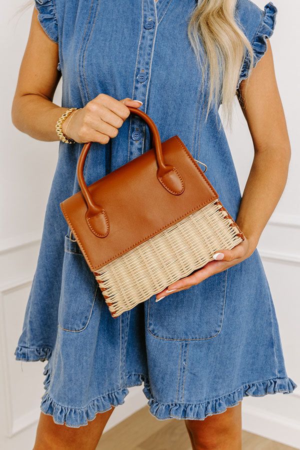 a woman wearing a denim dress and holding a brown handbag with wicker handles