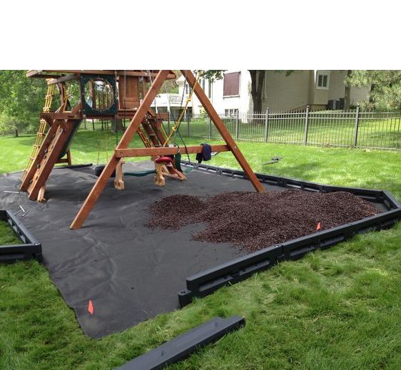 a play set in the grass with some dirt on it and a swing set behind it