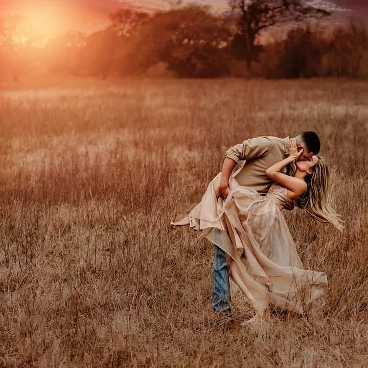 a man and woman are kissing in the middle of an open field with sunset behind them