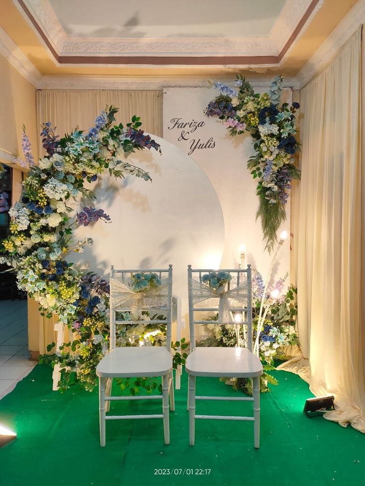 two white chairs sitting next to each other in front of a wall with flowers on it