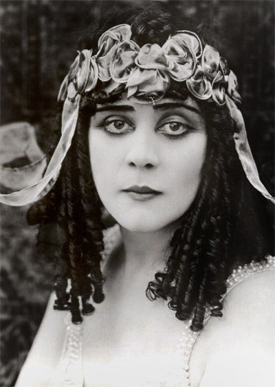 an old photo of a woman with braids in her hair wearing a headdress