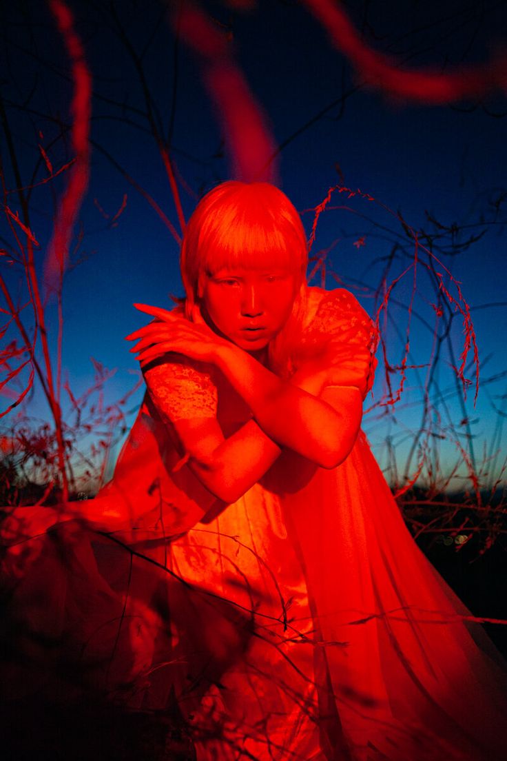 a woman in a red dress sitting on the ground with her arms crossed and looking at the camera