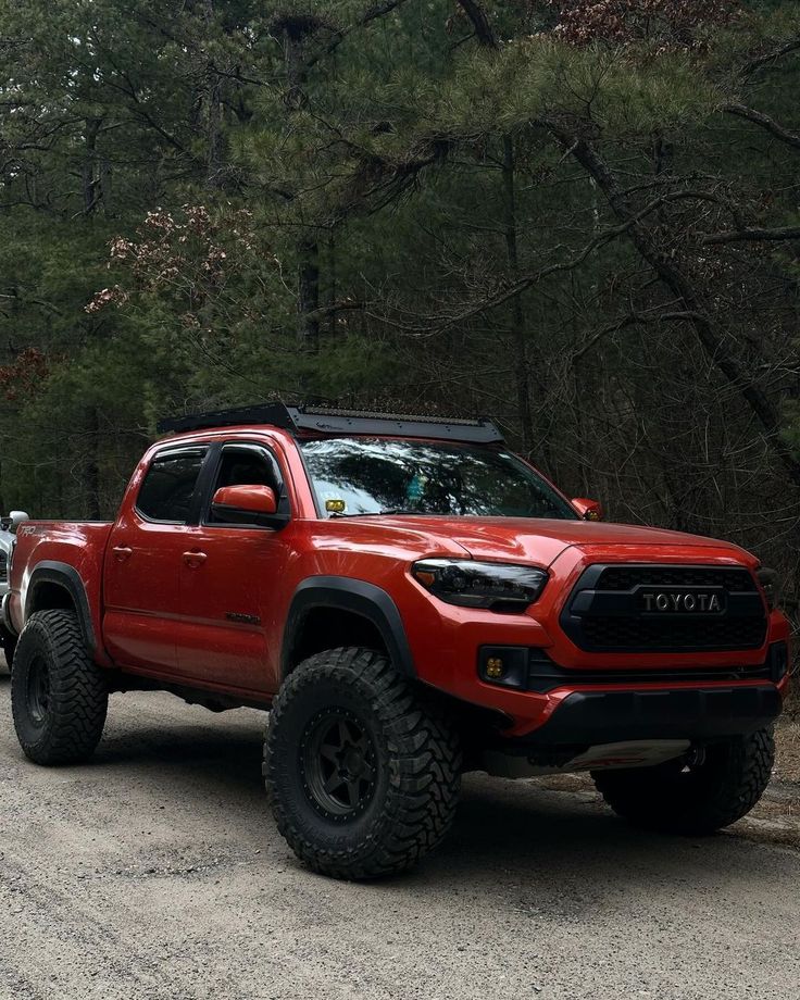 a red truck parked on the side of a dirt road next to some tall trees