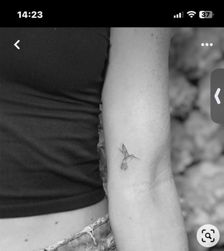 a black and white photo of a woman's arm with a small bird tattoo on it