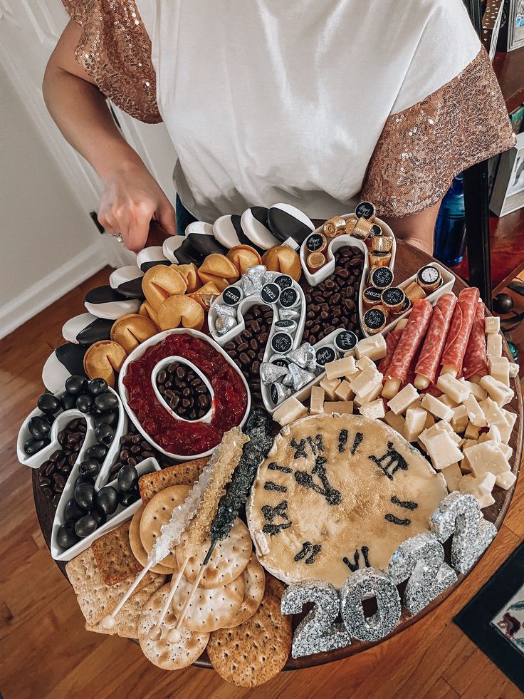 a woman standing in front of a platter filled with cheeses and crackers