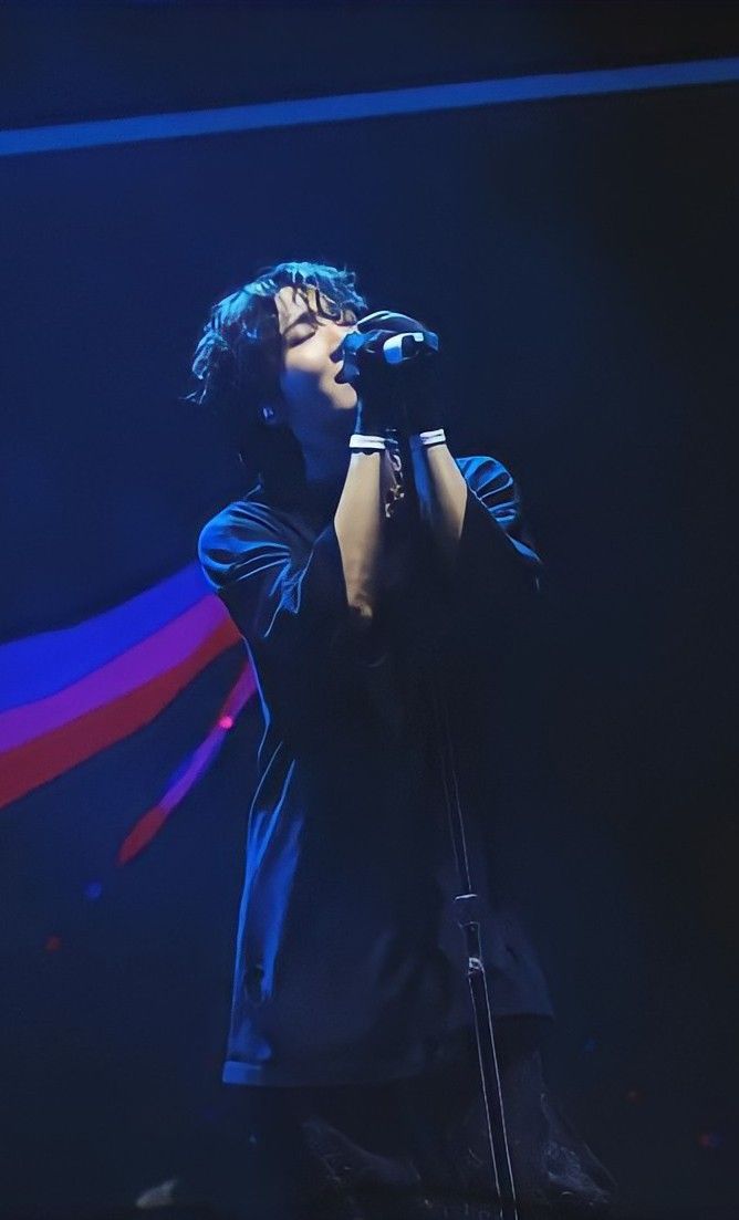 a man standing on top of a stage holding a microphone in his hand and singing