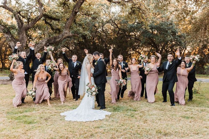 a large group of people in formal wear posing for the camera with their hands up