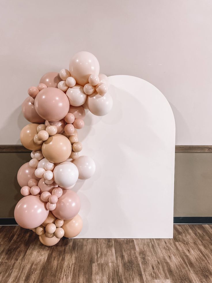 a bunch of balloons floating in the air on top of a wooden floor next to a white wall