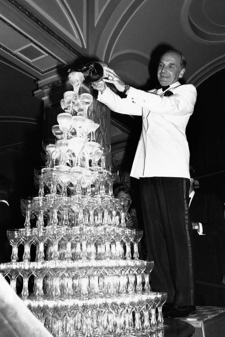 a man standing next to a large stack of wine glasses on top of a table