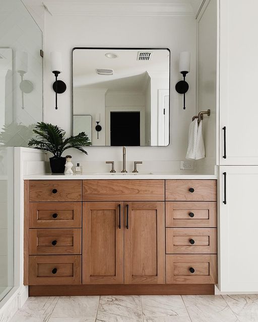 a bathroom with wooden cabinets and a large mirror above the sink, along with a plant