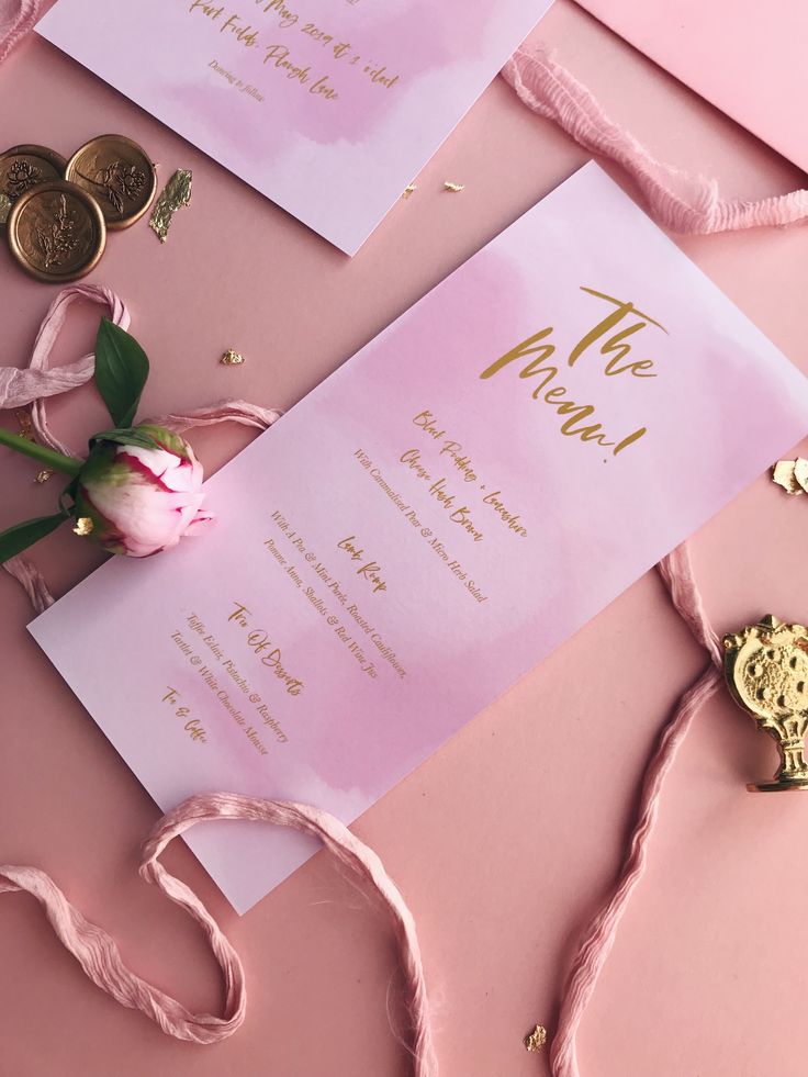 the wedding stationery is laid out on top of pink paper with gold foil lettering