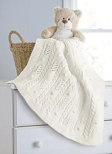 a teddy bear sitting on top of a white blanket next to a basket and window