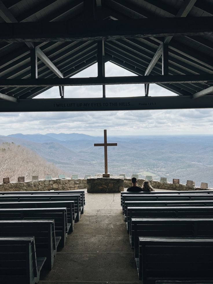 two people sitting at the end of pews with a cross in the background on top of a hill