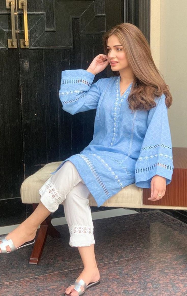 a woman sitting on top of a bench in front of a door with her legs crossed