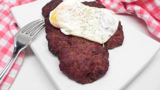 a white plate topped with meat and an egg on top of it next to a fork