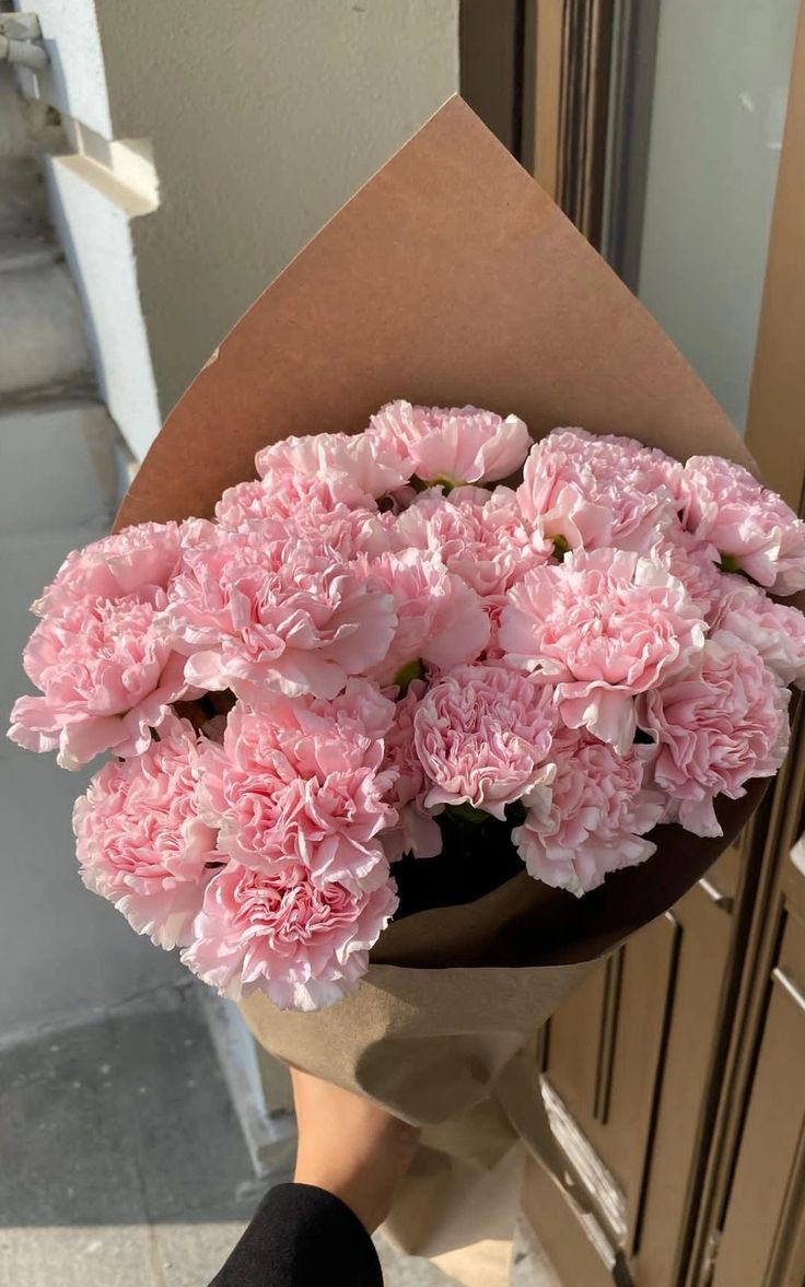 a person holding a bouquet of pink carnations in front of a building door