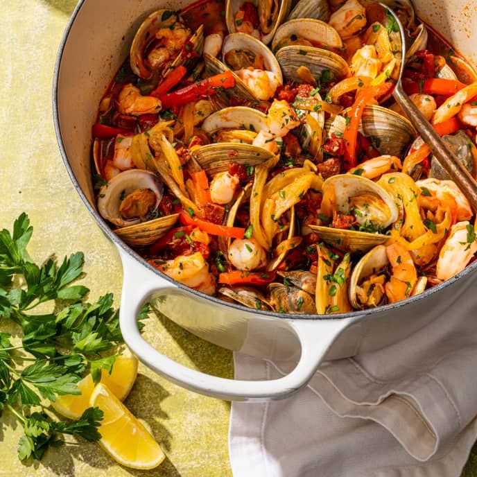 a pan filled with clams and vegetables on top of a table next to lemon wedges