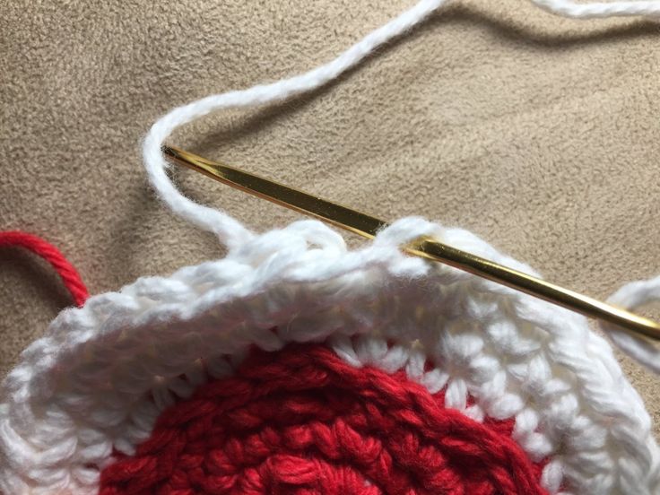 a crocheted red and white object with a gold knitting needle in it's center