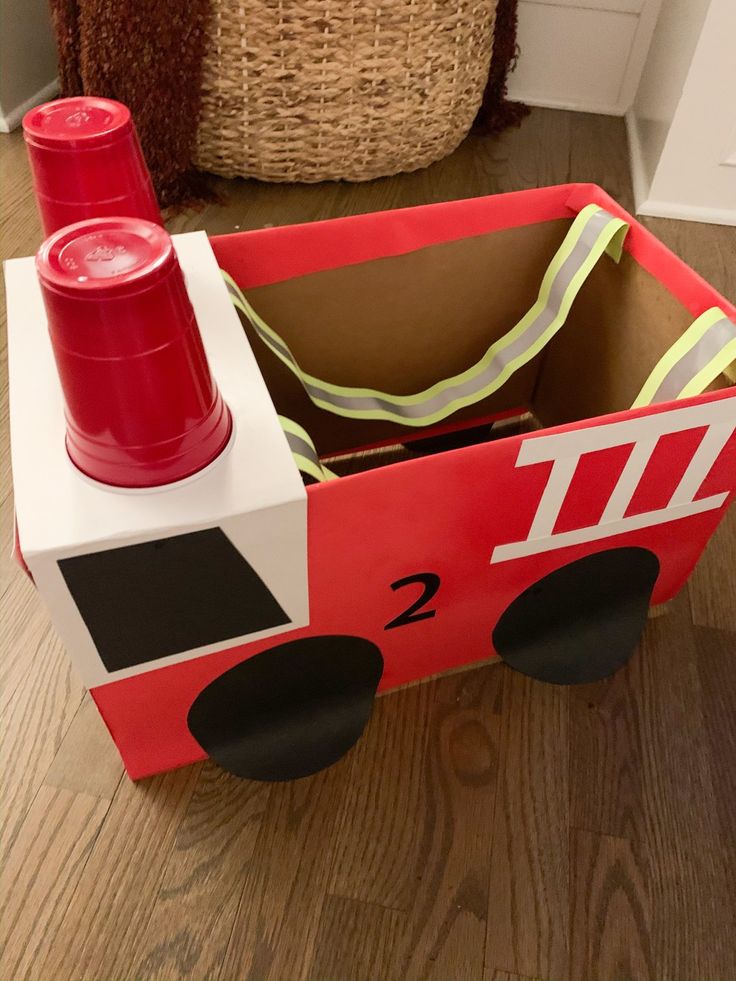 a cardboard fire truck sitting on the floor next to a basket with a red can in it