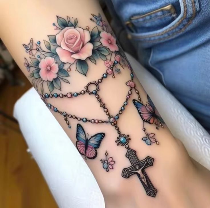 a woman's arm with tattoos on it and butterflies around the cross, roses and beads