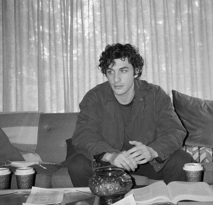 a black and white photo of a man sitting on a couch in front of a book