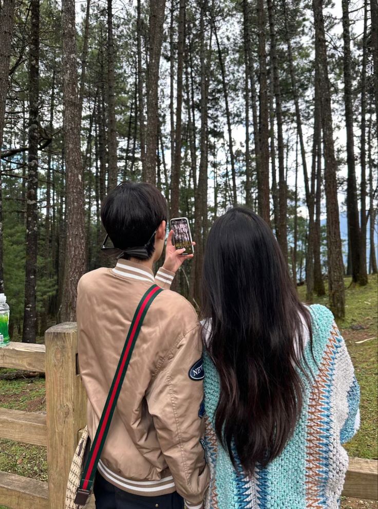 two people standing next to each other in the woods