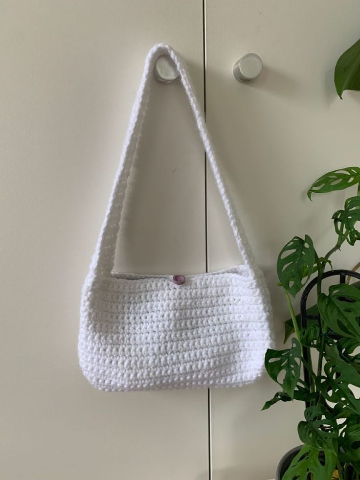 a white crocheted purse hanging on the wall next to a potted plant