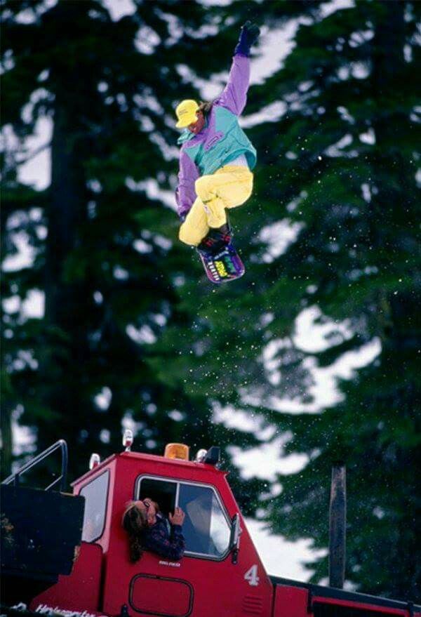 a man flying through the air while riding a snowboard in front of a red truck