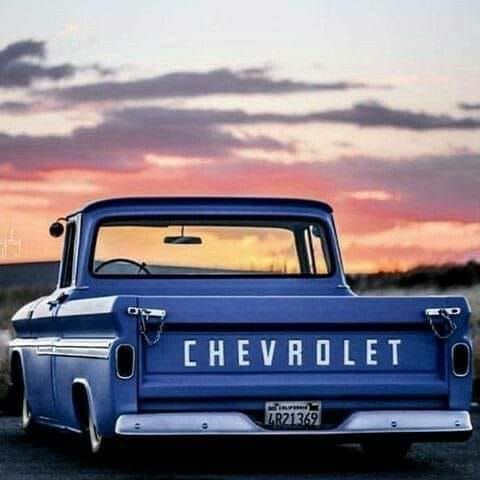 an old blue chevrolet pickup truck parked on the side of the road at sunset with clouds in the background