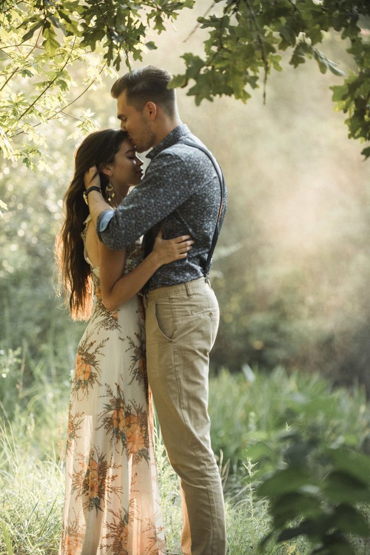 a man and woman embracing under a tree in the woods during their engagement photo session