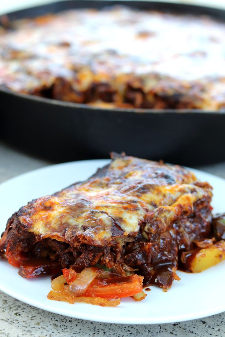 a piece of lasagna on a white plate next to a skillet dish