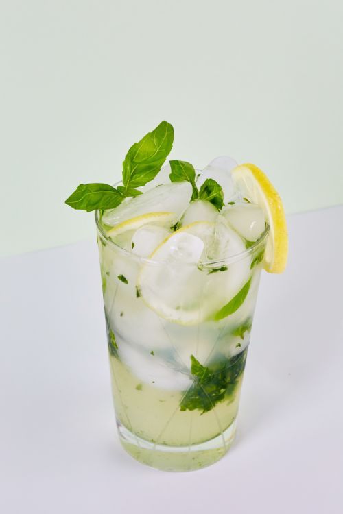 a mojito with mint and lemon on a white table next to a lime slice