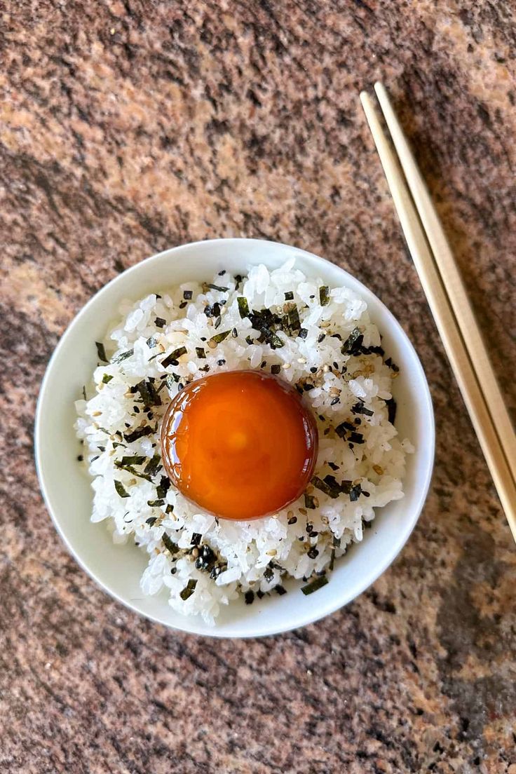 a white bowl filled with rice and sauce next to chopsticks