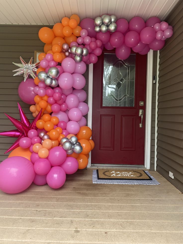 a bunch of balloons that are on the front steps of a house with a red door