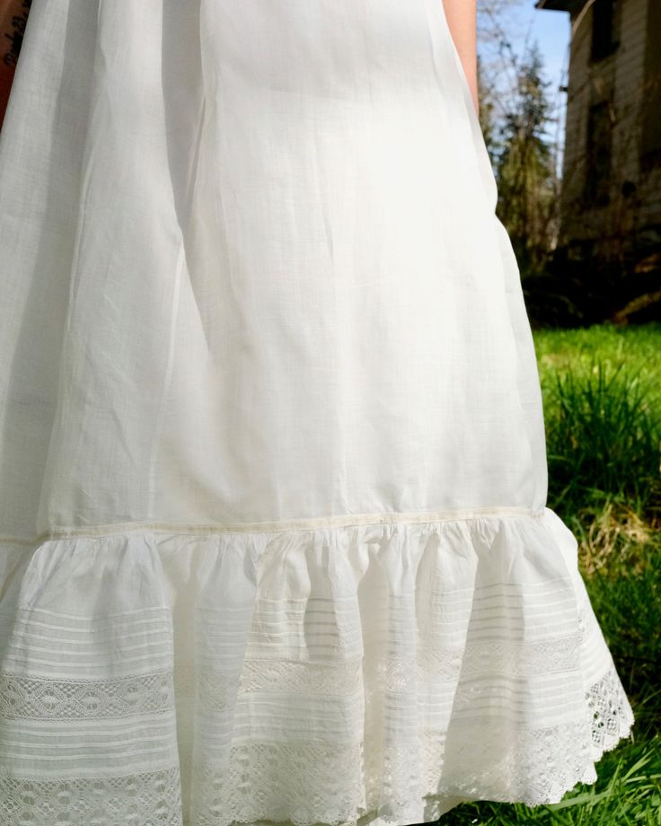 "Antique petticoat with 22\" waist. White cotton with smooth touch and light crispness. Flounce at hem with pin tucks and lace trim. Pale yellow and white ribbon detail at top of flounce. Single button closure at back with \"cheat\" string loop for an additional inch. Flat front waist with tight gathers at back. Very good condition, some small rust spots found on flounce (see last photo for example of majority of it). Measures 34\" long." Daywear Ruffled Petticoat, Daywear Tiered Petticoat With Ruffles, Daywear Tiered Skirt Petticoat With Ruffles, Daywear Ruffled Tiered Skirt Petticoat, Regency Style Ruffled Petticoat For Daywear, Vintage Petticoat With Attached Cancan For Summer, White Regency Style Petticoat With Ruffles, Vintage Lace Trim Petticoat For Summer, Vintage Petticoat For Summer Daywear