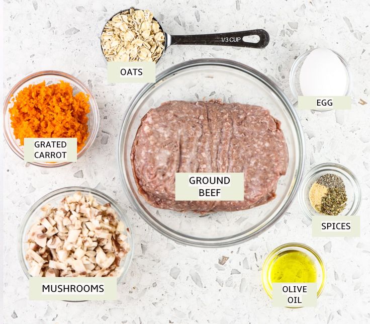 ingredients for ground beef are shown in bowls on a white counter top, including carrots, mushrooms, eggs, and seasonings