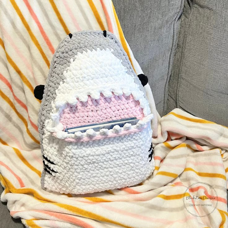 a crocheted backpack sitting on top of a couch next to a striped blanket