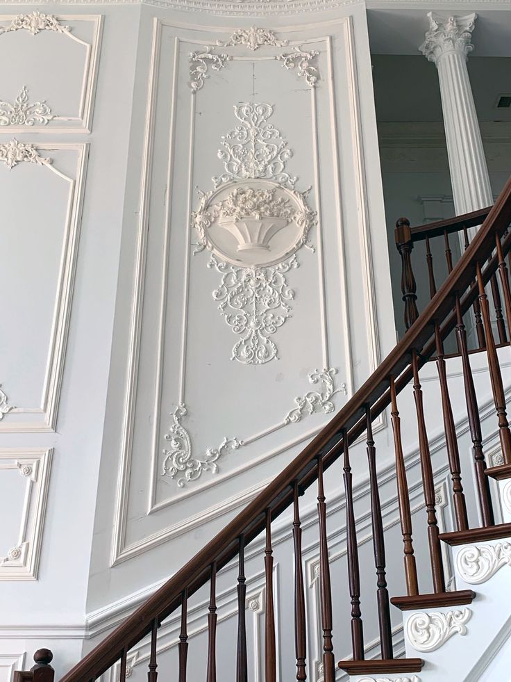 an ornately decorated stair case in a white room with wood handrails and decorative paneling