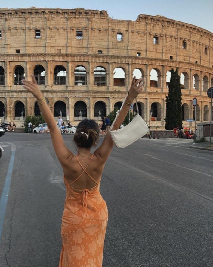 a woman in an orange dress is holding her arms up and looking at the roman colossion