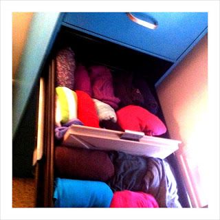 an open drawer filled with lots of different colored clothes and pillows on top of it