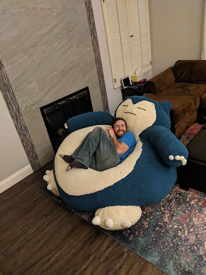 a man laying on top of a giant blue cat couch in a living room next to a fireplace